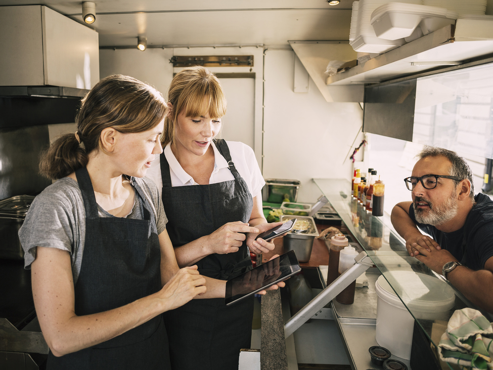 Two food truck owners taking an order from a customer. 