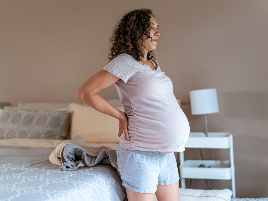 pregnant woman getting up out of bed and holding her back 