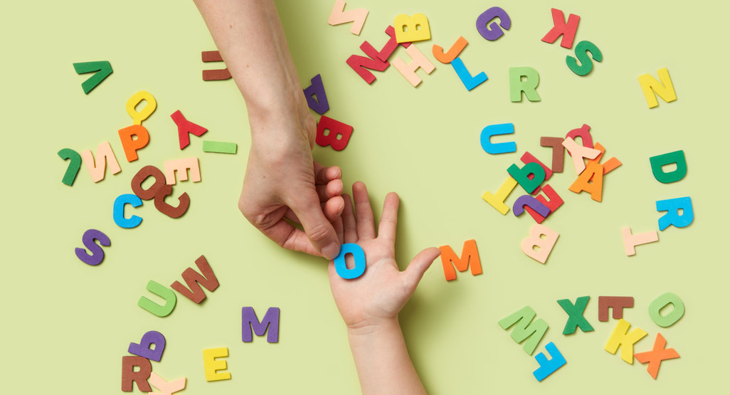 An adult hand passing a letter O to a child's hand surrounded by other printed letters