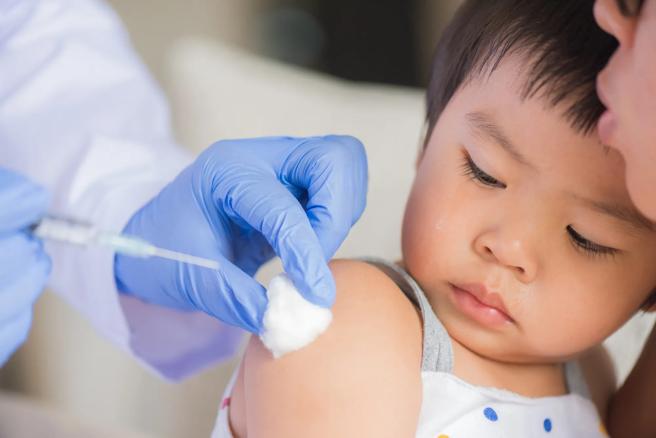 Gloved hands of healthcare provider giving a shot in the shoulder of a young child