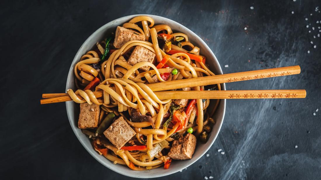 Bowl of soba noodles with veggies and tofu, with chopsticks across top of bowl