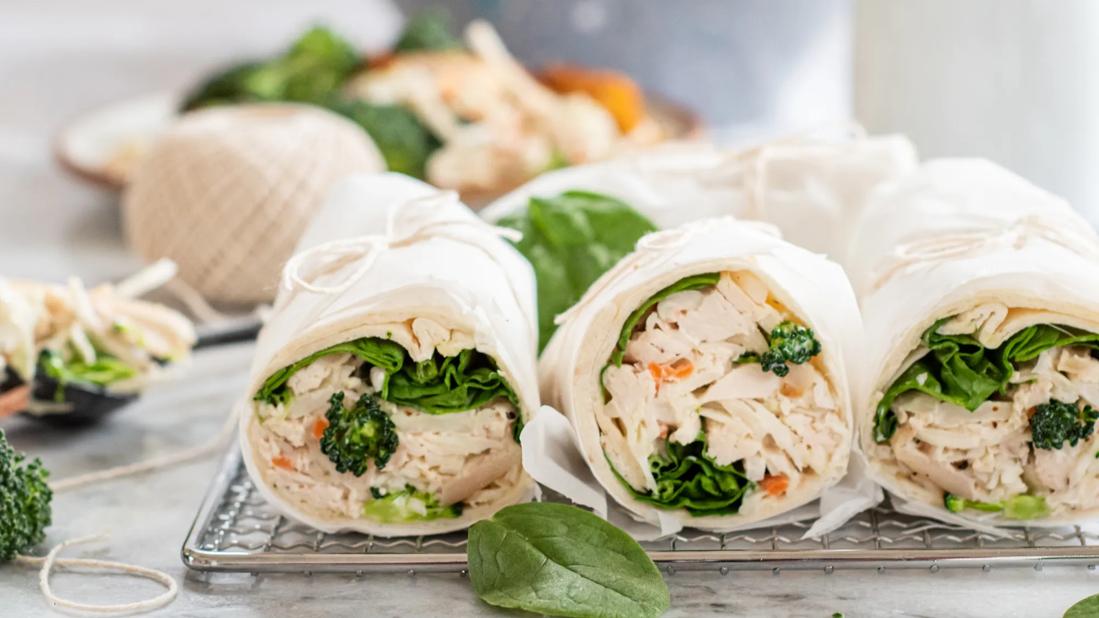 Broccoli slaw chicken wraps wrapped in paper, tied with string on cooling rack on counter