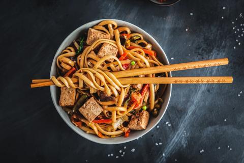 Bowl of soba noodles with veggies and tofu, with chopsticks across top of bowl