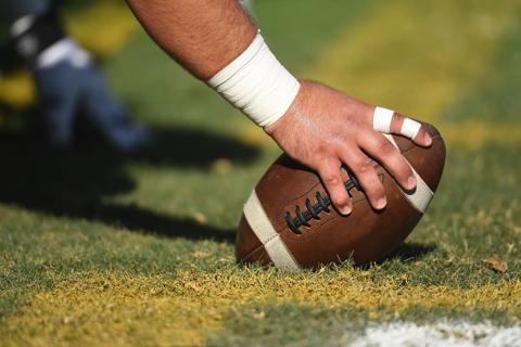 Large hand with athlete-taped wrist and fingers gripping football on the field