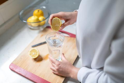 Person squeezing half a lemon into a glass of water