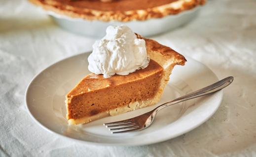 Slice of pumpkin pie with dollop of whipped topping on white plate with fork