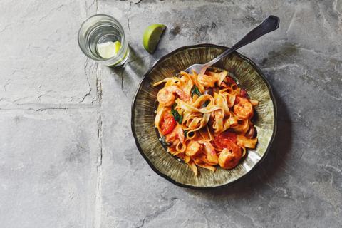 Italian pasta with shrimp in bowl with fork, glass of lime water next to, on stone table