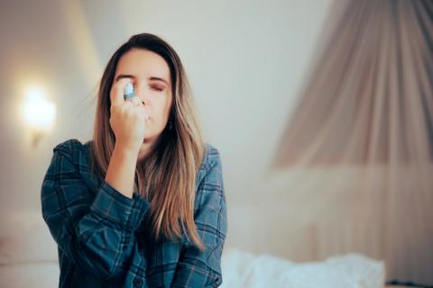 Person with eyes closed, inhaling on an asthma inhaler