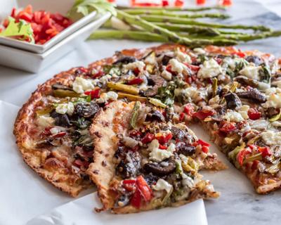 Whole arugula, veggie and goat cheese pizza, with one piece cut, with asparagus in background