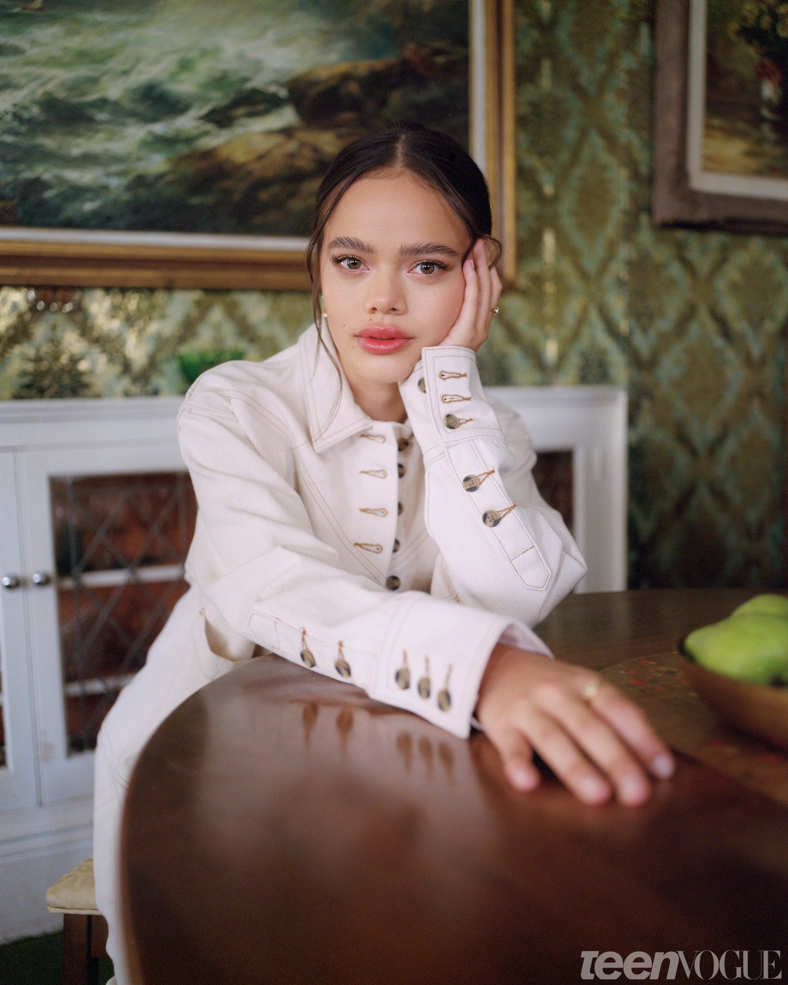 Malia close up with chin on her hand seated at a dark wood table