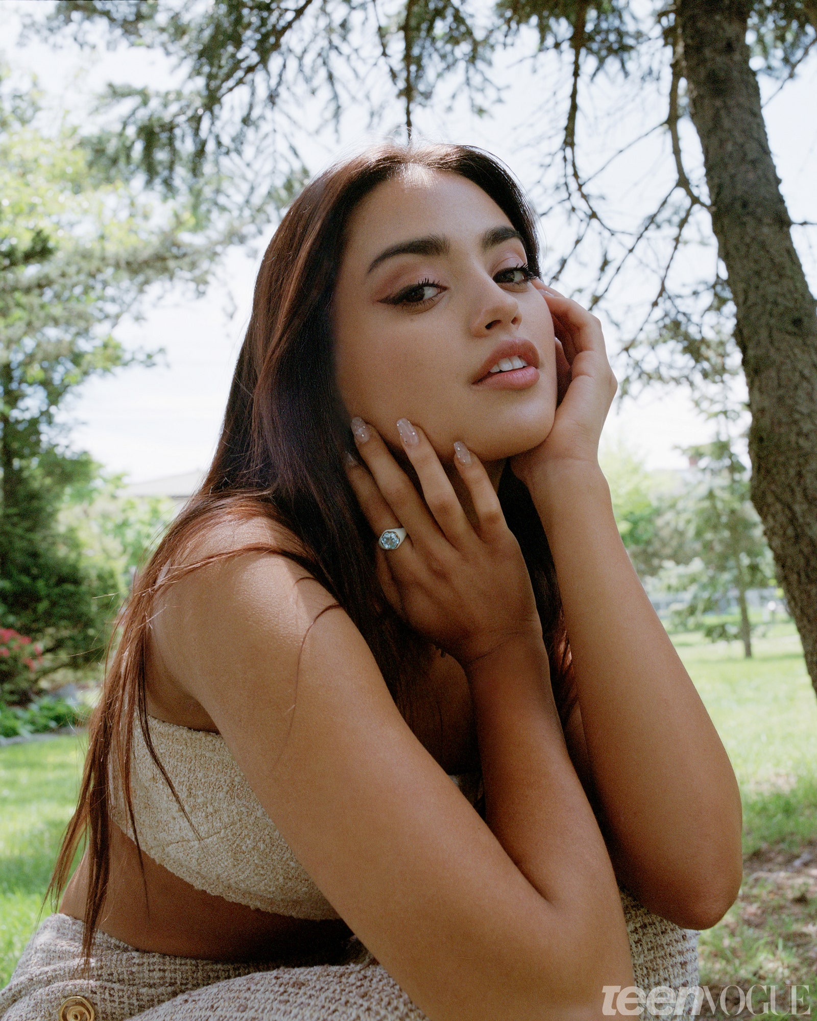 Maia kneeling outside with her hands posed artfully around her face