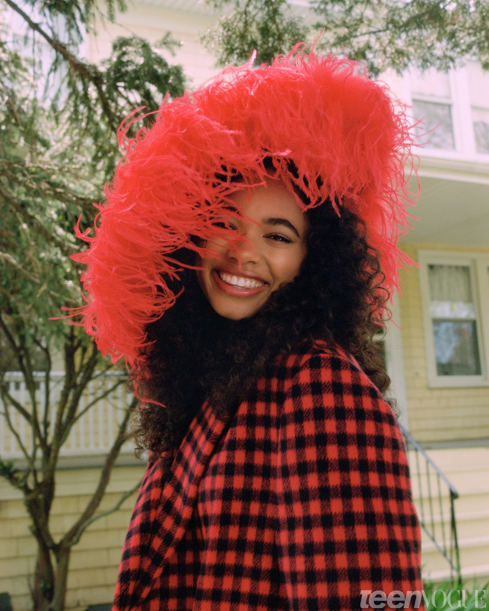 Chandler Kinney close up in red and black plaid with big red feathered hat