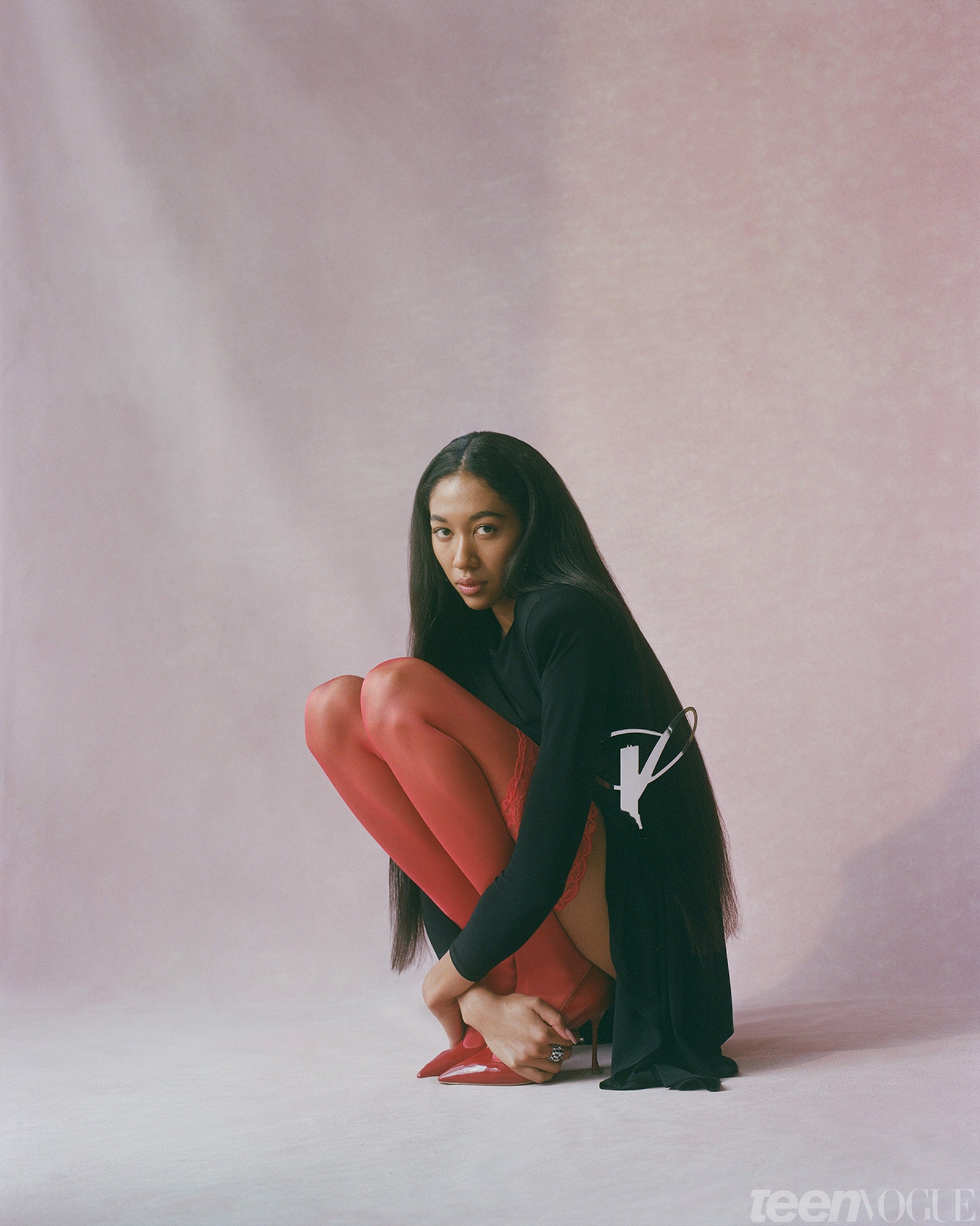 Aoki Lee Simmons sitting in black dress and red tights.