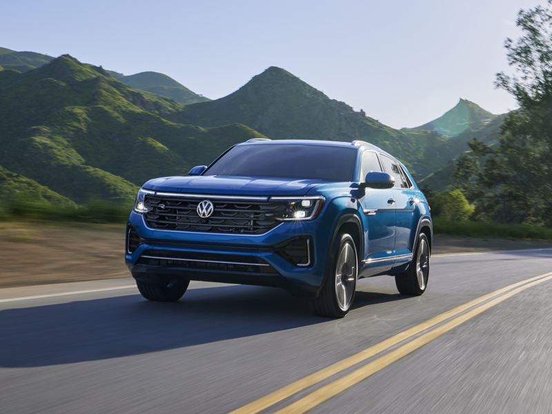 Front view of an Atlas Cross Sport shown in Kingfisher Blue Metallic driving on a wooded mountain road.