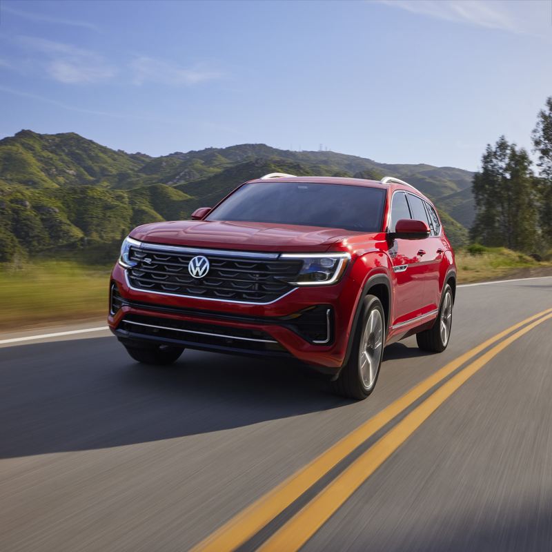 Front view of an Atlas shown in Aurora Red Metallic driving on a wooded mountain road.