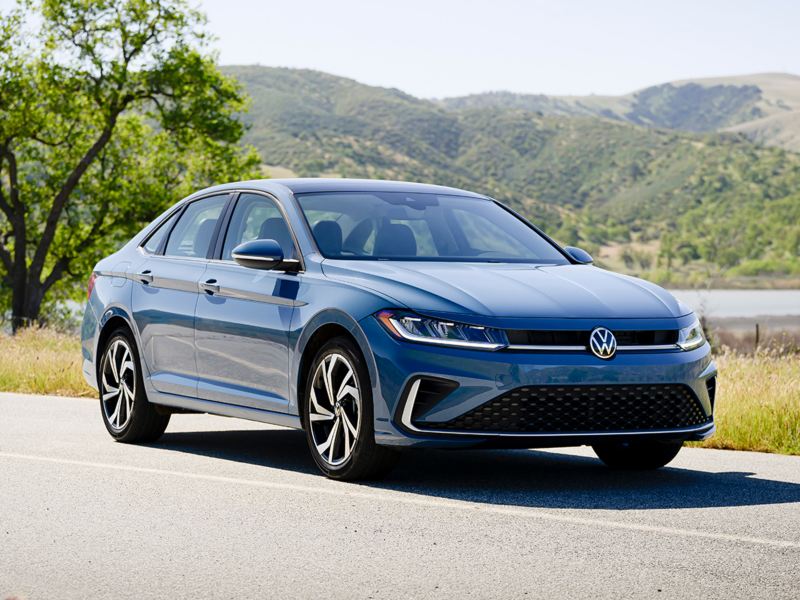 Front ¾ view of a Jetta shown in Monterey Blue Pearl with wooded hills in the background.