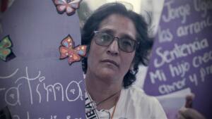 Lorena gazes out form between large lavender signs with butterflies at what seems to be a demonstration