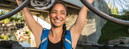 A cyclist wearing a hydration backpack lifts a road bike triumphantly over her head