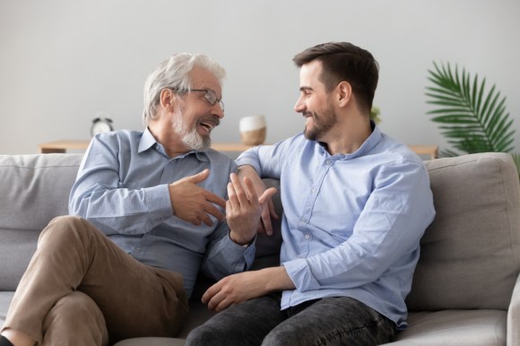 Older man with his adult son sitting on the couch conversing.