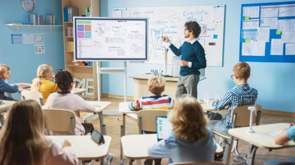  Male teacher standing at the front of the class teaching on digital whiteboard.