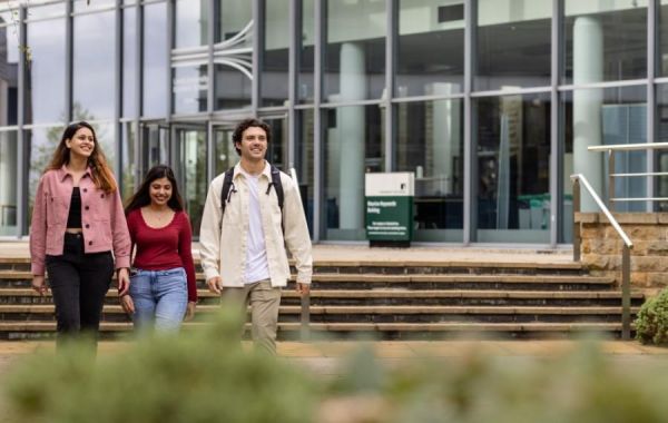 Three students walking outside glass-fronted building