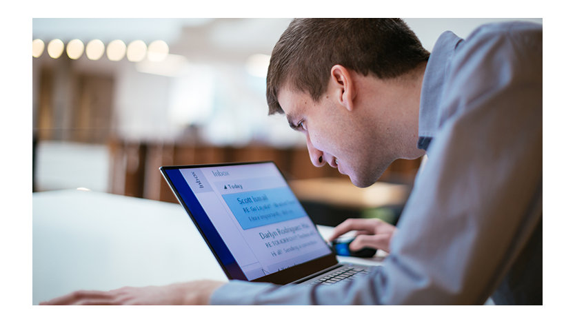 A man who has low vision, looks closely at a laptop with magnified text to view the screen