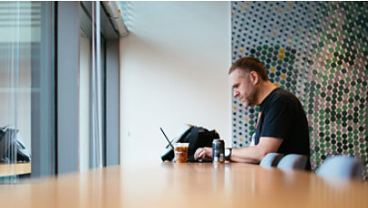 A man with a social disability, sits alone in the corner of an office building and works on a laptop.