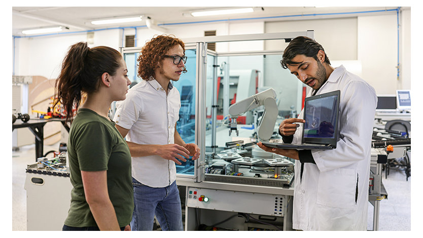 People discussing in a lab with a robotic machine in the background.