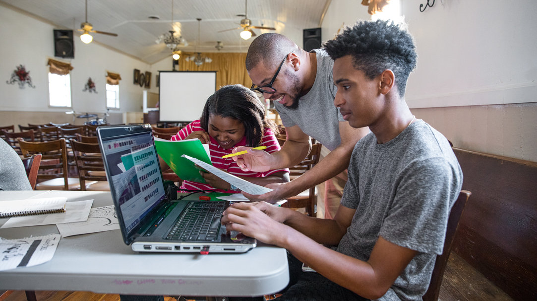 Three people taking notes and typing on a laptop