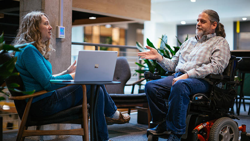 Stuart Pixley, a man who uses a wheelchair, talks to a colleague in the lobby of an office building.