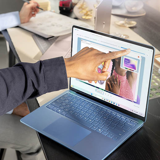 A hand touches the Surface Laptop screen to edit a PowerPoint presentation. 