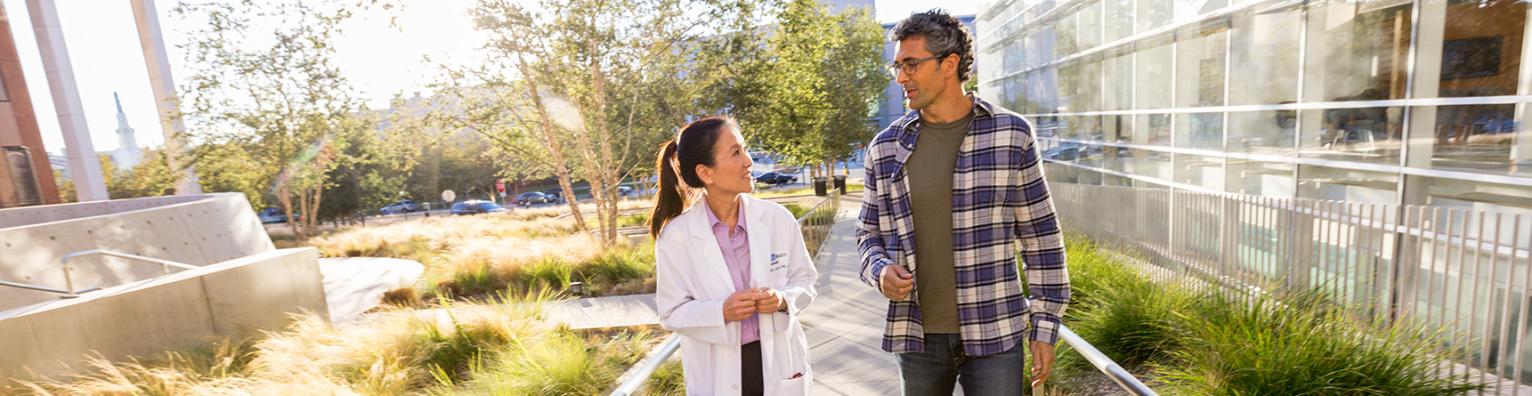 Female physician walking outside of medical building with male patient