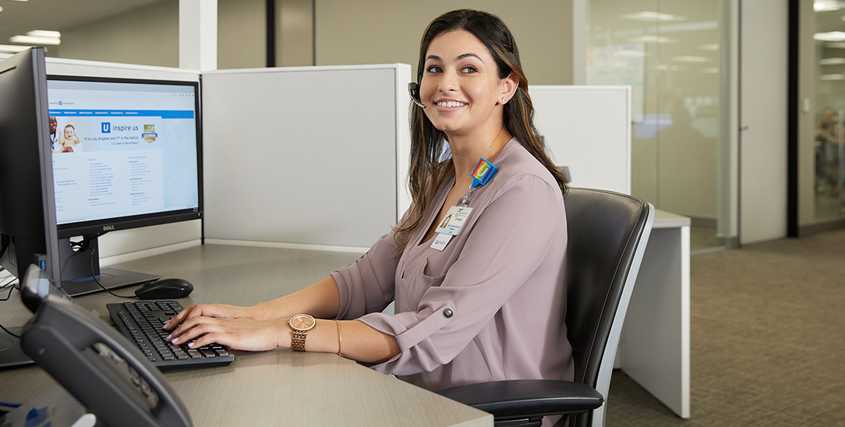 Female administrative support professional with headset at desk in cubicle