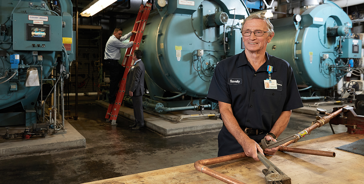 Male facilities maintenance professional holding tools in front of large machinery