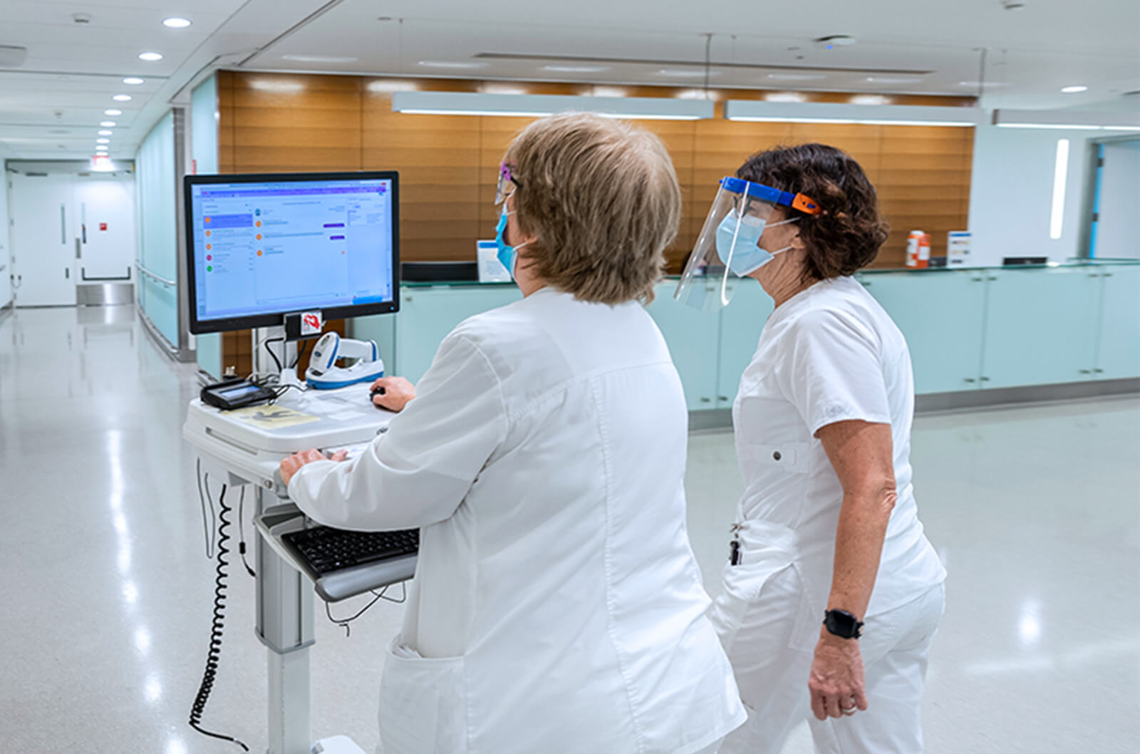 Masked medical professionals working at a rolling computer station