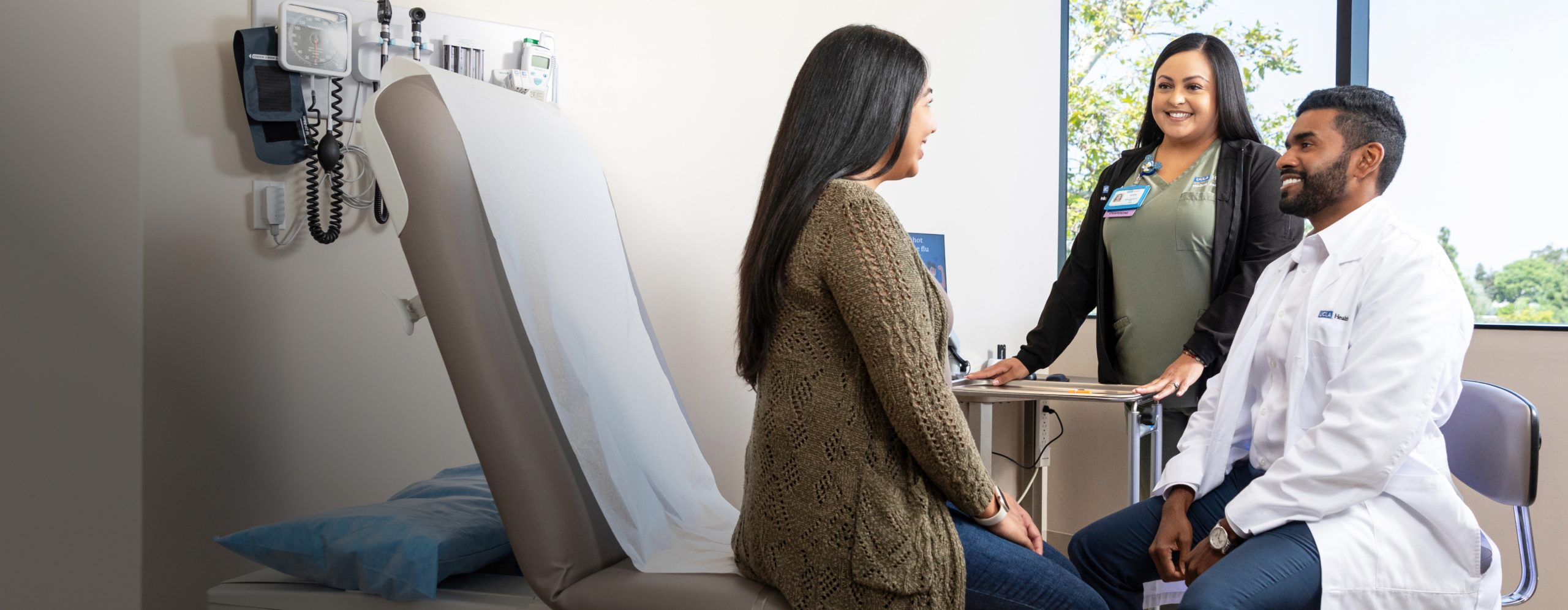 Two UCLA Health clinical professionals consulting with a female patient at the bedside of a hospital room