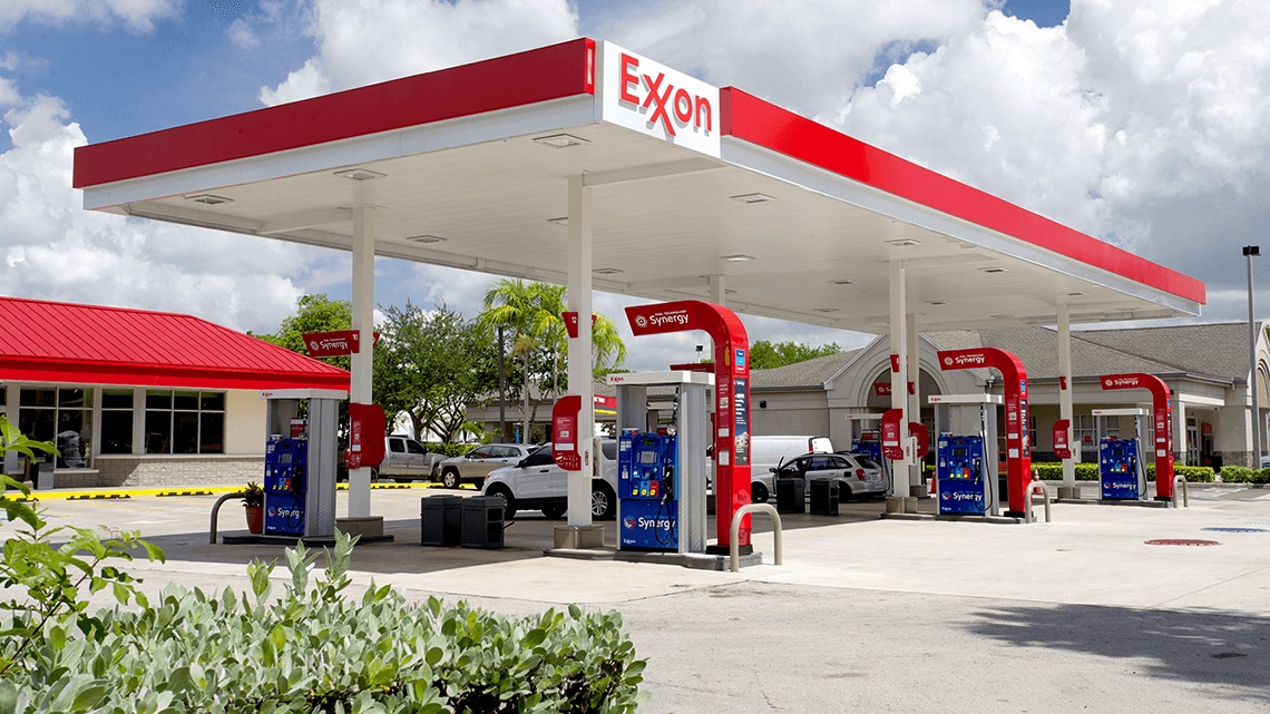 Exxon Mobil gas station with multiple gas pumps, a white car is at one pump, sunny day with white puffy clouds