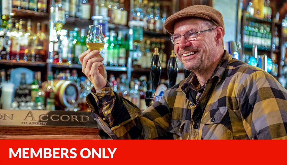 ralfy mitchell sitting at a bar holding a whisky glass; red members only banner at bottom