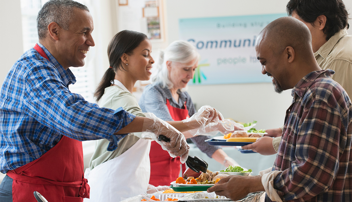 Three volunteers serving food to two men at a community kitchen