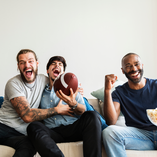 Three men cheer for their football team while watching a game at home.