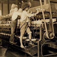 Young boys working in a thread spinning mill in Macon, Georgia, 1909. Boys are so small they have to climb onto the spinning frame to reach and fix broken threads and put back empty bobbins. Child labor. Industrial revolution