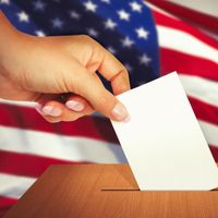 Close up of a hand placing a ballot in a ballot box. Election vote voter voting