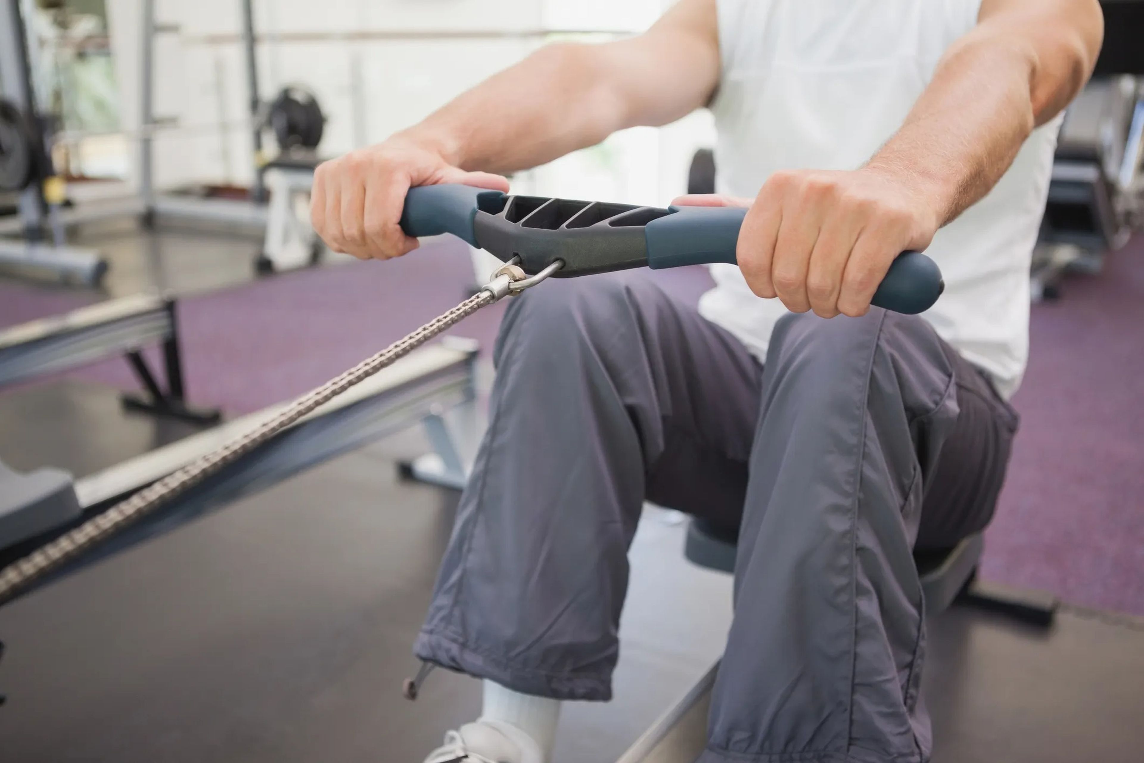 A close up of a man's hands gripping the handle of a rowing machine in a gym