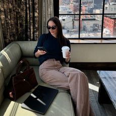 Fashion influencer Liv Perez sitting by a window with the view of New York City wearing a chic fall outfit.