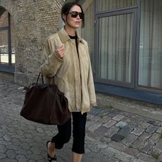 Annabel wears a suede jacket, brown oversize bag, black capri pants, and sandals.