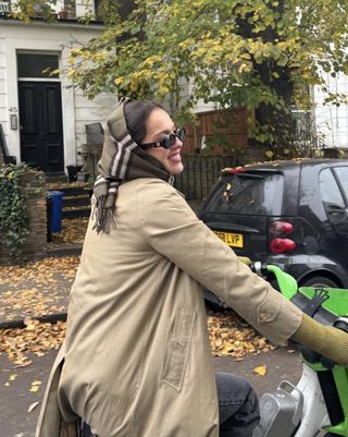 Olivia Rodrigo riding a bike in London wearing a Burberry scarf on her head with a Burberry trench coat and sunglasses.