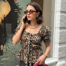 Influencer wears a leopard print puff-sleeve top, a chain necklace, gold earrings, and sunglasses.