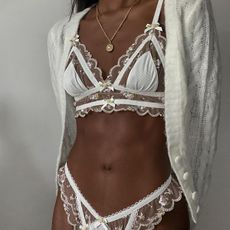 a close photo of a woman wearing one of the best lace bras in the form of a white bralette with sheer lace styled with a gold chain and white cardigan