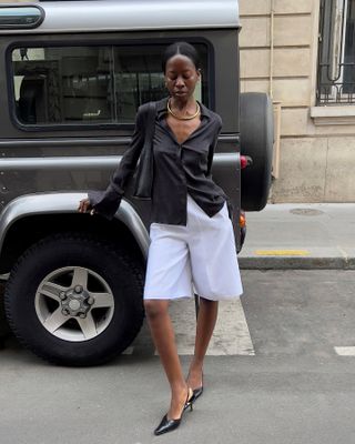 Woman wearing a black top, long white shorts, and heels.