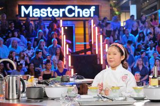 a young girl standing in front of a kitchen counter with an audience behind her on MasterChef Junior